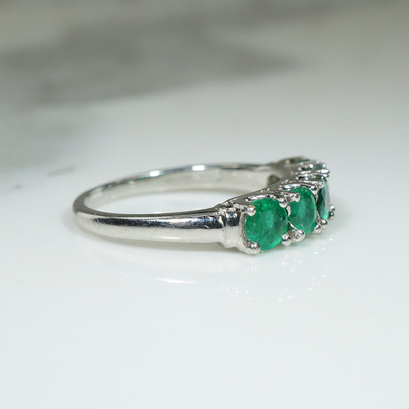 platinum band ring with five green emerald stones on a white background