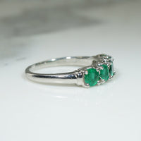 platinum band ring with five green emerald stones on a white background