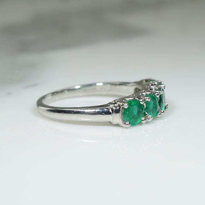 platinum band ring with five green emerald stones on a white background