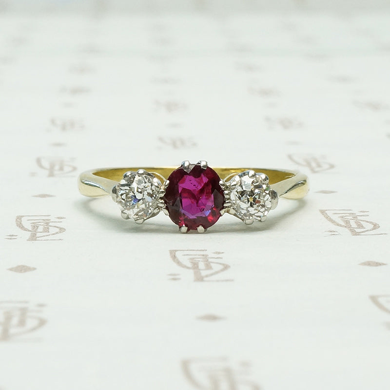 old mine cut diamonds sit to either side of a rich red oval ruby the 3 stone setting is platinum on 18k yellow gold