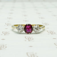 old mine cut diamonds sit to either side of a rich red oval ruby the 3 stone setting is platinum on 18k yellow gold