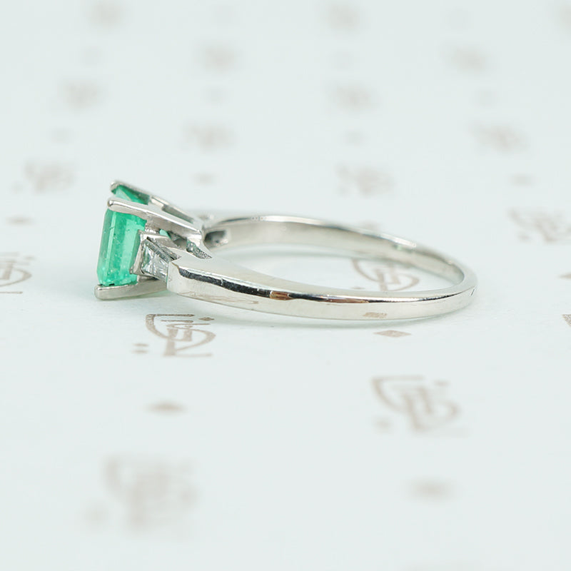 Square green emerald in platinum engaement ring with diamond baguette sides side view of diamonds
