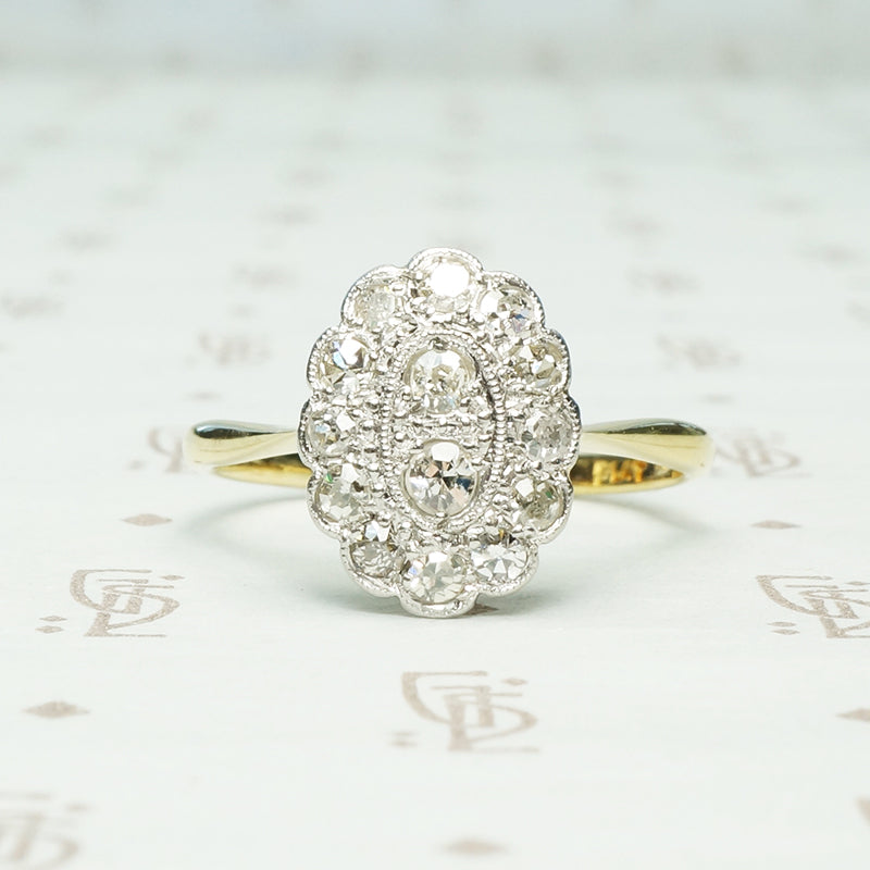 large oval halo of diamonds in platinum surround 2 diamonds at the center atop an 18k yellow gold setting