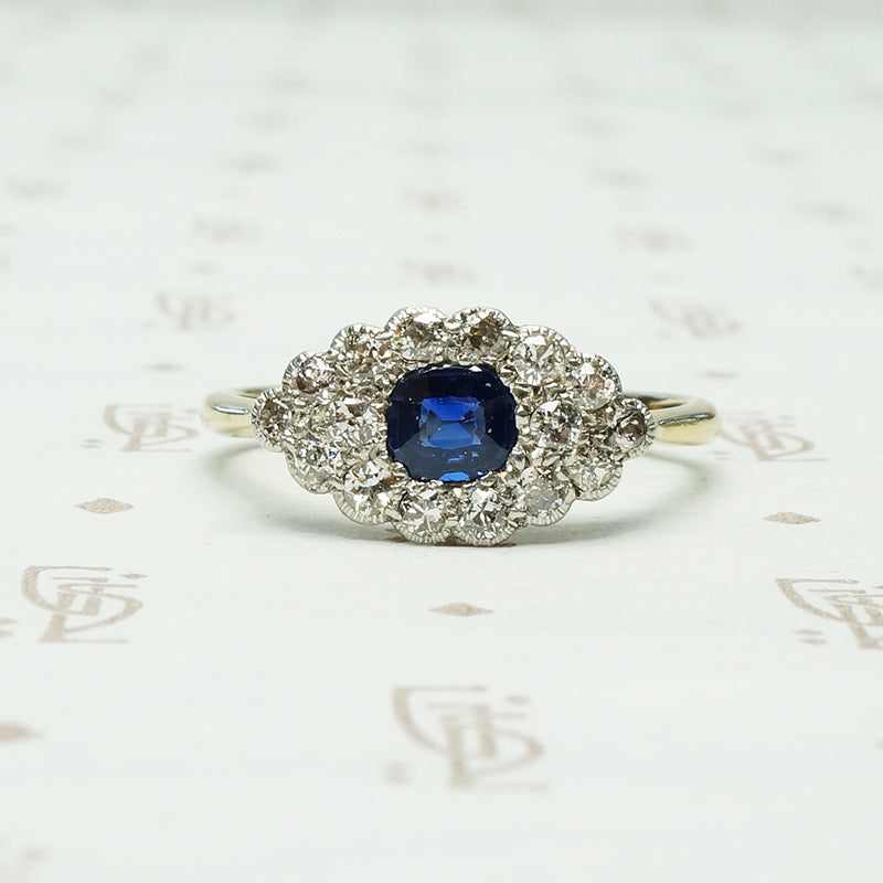 a cushion cut indigo blue natural sapphire is set east west amid a group of diamonds in an eye shaped platinum on 18k yellow gold ring