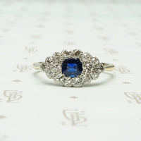a cushion cut indigo blue natural sapphire is set east west amid a group of diamonds in an eye shaped platinum on 18k yellow gold ring