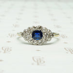 a cushion cut indigo blue natural sapphire is set east west amid a group of diamonds in an eye shaped platinum on 18k yellow gold ring