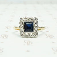 an emerald cut .60ct inky blue sapphire framed by diamonds in 18k yellow gold and platinum