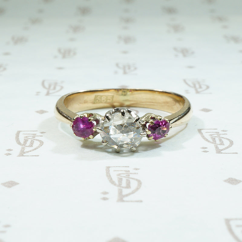 oval natural red rubies are set to either side of a round rose cut diamond in 14k gold