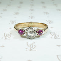 oval natural red rubies are set to either side of a round rose cut diamond in 14k gold