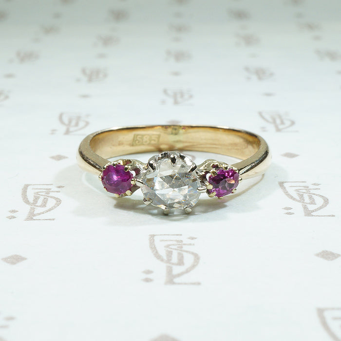 oval natural red rubies are set to either side of a round rose cut diamond in 14k gold